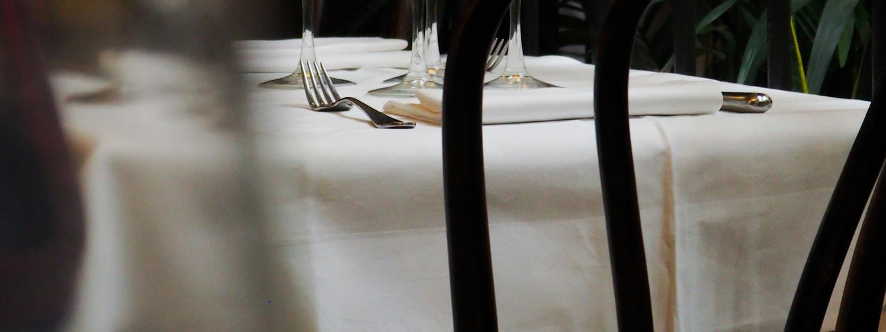 A restaurant table laid with white linen and cutlery.