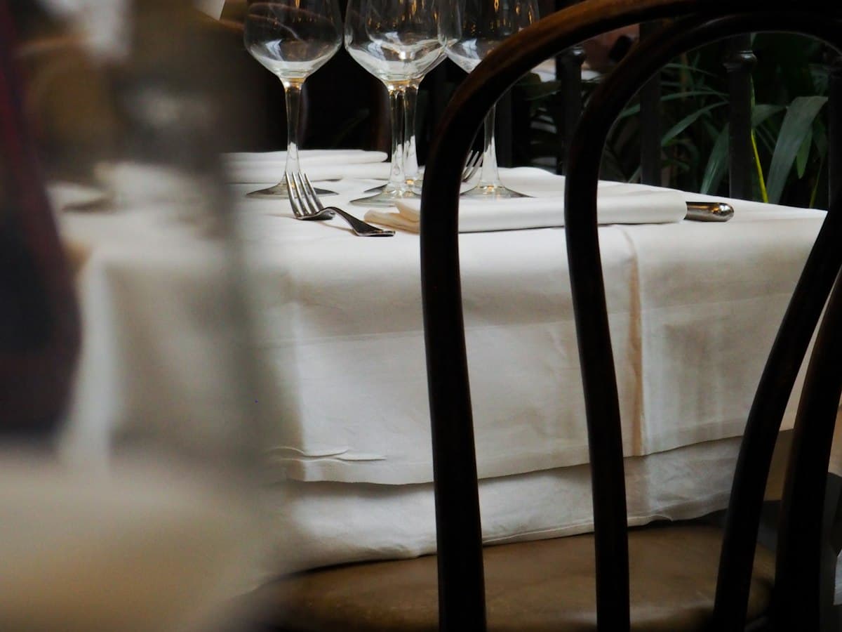 A restaurant table laid with white linen and cutlery.
