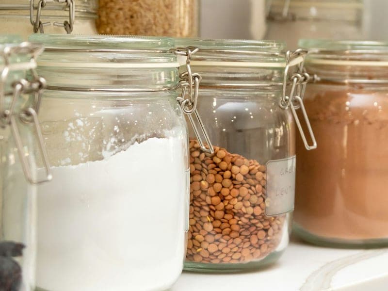 Labelled storage jars of flour, lentils and cocoa on a shelf.