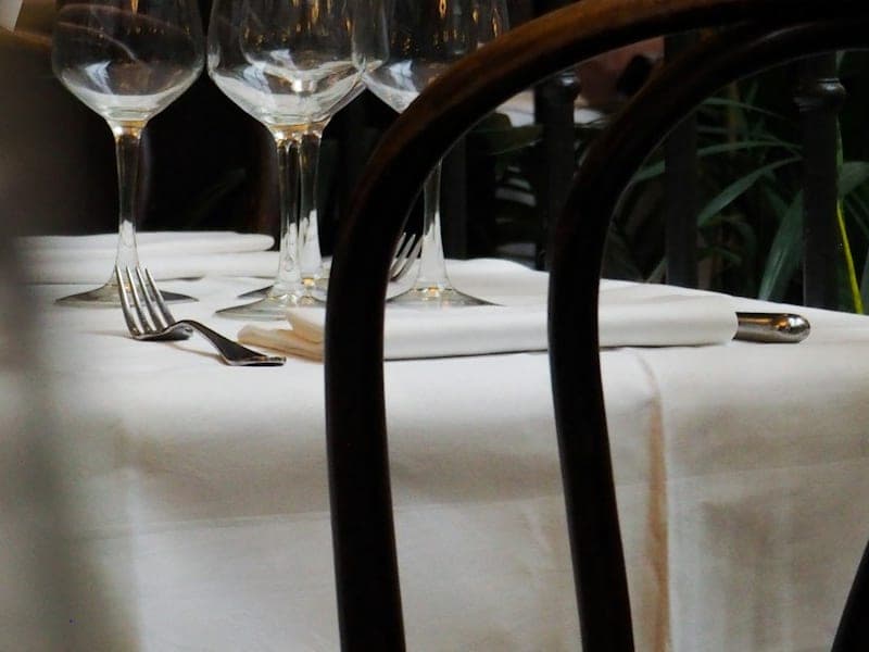 A restaurant table laid with white linen, wine glasses and cutlery.